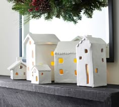 three white houses sitting on top of a mantle next to a christmas tree and wreath