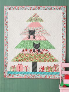 a quilted christmas tree hanging on the wall next to a pink chair and table