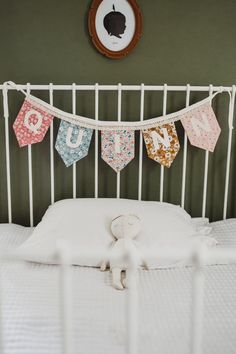 a white bed topped with a stuffed animal next to a wall hanging from a metal headboard