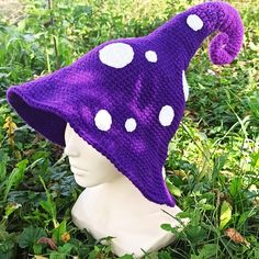 a purple and white knitted hat with polka dots on it sitting in the grass