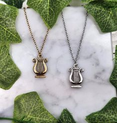 two gold and silver necklaces sitting on top of a white marble table next to green leaves