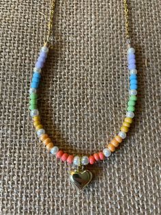 From Saltair Bead Studio, a simple pastel rainbow necklace with a gold heart charm.  Length: 17 inches. Slightly longer than a typical choker, and will lay nicely around the base of your neck. **If you need a different length or clasp for fit and/or accessibility, please let me know and I am happy to create a custom order** Hand-strung with czech and toho glass beads, enamel/metal charm, gold-colored chain, and a lobster clasp. All metal is lead and nickel free. Each necklace is unique and may vary slightly due to variations in bead size.  I want you to be 100% happy with your purchase and pride myself in great customer service! Please reach out if you have any questions or concerns. Want to see what new creations will soon be arriving in Saltair Bead Studio? Follow me on tiktok or instagr Trendy Multicolor Heart Charm Necklace, Trendy Gold Beaded Necklaces With Heart Beads, Trendy Gold Beaded Necklace With Heart Beads, Multicolor Heart Charm Necklaces With Heart Beads, Trendy Rainbow Necklace With Heart Beads, Trendy Rainbow Necklaces With Heart Beads, Bead Studio, Rainbow Necklace, Rainbow Heart