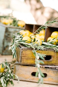 two wooden crates filled with lemons and green leaves on top of a table next to other fruit