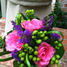 a bouquet of pink and purple flowers sitting on top of a brick floor next to a planter