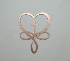 a heart with a cross hanging from it's side on a gray wall in front of a grey background