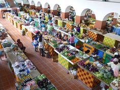 an indoor market filled with lots of people shopping for fruits and vegtables