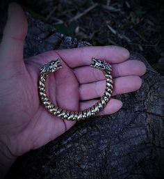 a hand holding a gold colored bracelet on top of a tree trunk in the dark