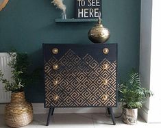 a black and gold cabinet in the corner of a room with two plants on it