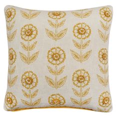 a white and gold pillow with yellow flowers on the front, sitting on a white surface