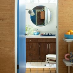 an open door leading to a bathroom with wooden cabinets and white tile flooring, along with a round mirror on the wall