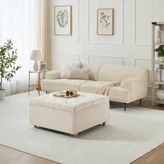 a living room with white walls and wooden flooring, a beige couch and ottoman in front of a large window