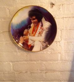 an elvis presley photo on a white brick wall with a gold rimmed plate hanging from the ceiling