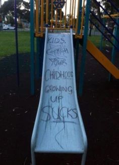 a slide with graffiti written on it in a park area next to a play structure