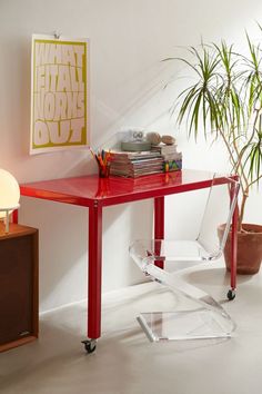 a red table with some books on it and a plant in the corner next to it