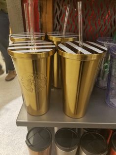 three starbucks cups sitting on top of a metal shelf next to other coffee mugs