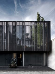 a black building with vertical glass on the front and side walls that are lined with plants