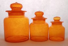 three orange glass jars with lids on each one are lined up against a white background