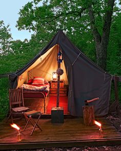 a tent is set up in the woods with two chairs and a bed on it