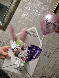 someone is holding a birthday card and some chocolates in a envelope with balloons on the wall