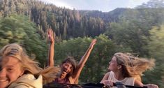 three girls are riding in a vehicle with their arms up and one girl is waving