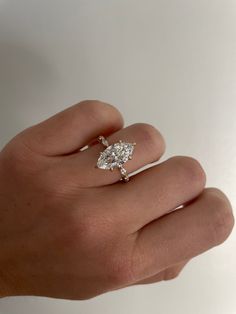 a person's hand holding a ring with a pear shaped diamond on top of it