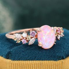 an opal and diamond ring sitting on top of a blue velvet cushion