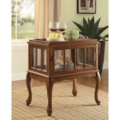 a small wooden table with glass doors on the top and bottom shelf holding wine glasses