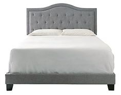 an upholstered bed with white sheets and pillows