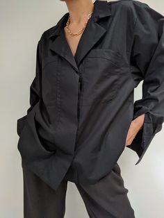 a woman standing in front of a white wall with her hands on her hips wearing a black shirt and pants