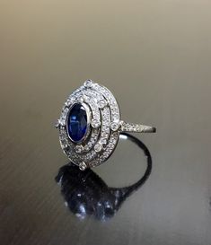 DeKara Designs Collection Art Deco Inspired Extremely Elegant Halo Sapphire Diamond Engagement Ring. Metal- 90% Platinum, 10% Iridium. Stones- 1 Oval Ceylon Blue Sapphire 1.25 Carats, 100 Round Diamonds F-G Color VS2 Clarity .80 Carats. Size- 6 1/4. An Amazing Art Deco Inspired Ceylon Blue Sapphire Triple Halo Diamond Engagement. The ring features a beautiful Ceylon Blue Sapphire that is expertly bezel set in the center. The sapphire is surrounded by 92 pave and burnish set round sparkling diamo Luxury Sapphire-colored Diamond Ring With Diamond Cut, Luxury Oval Diamond Cut Sapphire Ring, Luxury Sapphire-colored Diamond Ring, Exquisite 14k White Gold Ring With Center Stone, Luxury Oval Sapphire Ring In Platinum, Baguette Cut Sapphire Jewelry For Wedding, Luxury Oval Cubic Zirconia Rings, Classic Platinum Gemstone Ring, Elegant Marquise Sterling Silver Ring