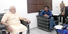 two men sitting in chairs talking to each other while another man sits on the floor