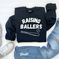 Show your baseball mom pride with our trendy "Raising Ballers" sweatshirt. This soft and cozy graphic tee is perfect for game day or any casual outing. Made from high-quality fabric, it offers comfort and style in one package. The bold design will make you stand out and show your love for baseball. Ideal for gifting, this sweatshirt is a must-have for any proud sports mom. Available in various sizes. Get yours today and enjoy cheering for your little ballers in style! Raising Ballers, Mom Pride, Baseball Sweatshirts, Mom Graphic Tees, Softball Mom, Sports Mom, Baseball Mom, Baseball Softball, Bold Design