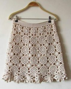 a white crocheted skirt hanging on a wooden hanger, with the bottom part off