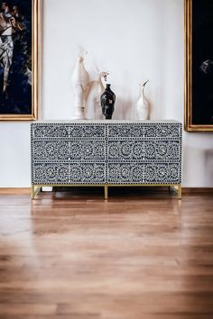 two vases sitting on top of a blue and white cabinet in front of paintings