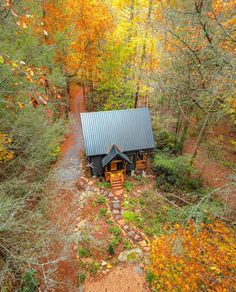 an aerial view of a small cabin in the woods surrounded by trees with yellow leaves