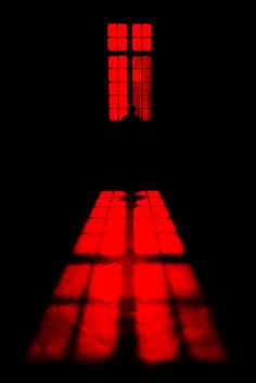 the shadow of a person standing in front of a window with red light coming from it