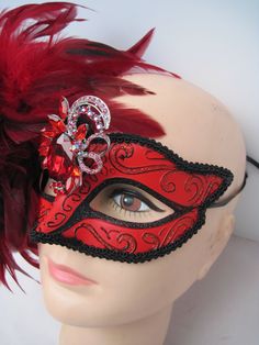 * Generous and red and black fluffy feathers over the right side of the face in this design. The feathers pick up the black braided trim around the mask and the black glitter eye liner. In addition the asymetrical faceted red crystal medallion adds more drama to the mask. * To secure the mask there are black satin ribbons to tie in the back of the head. The ribbons can be cut as I always include plenty of length. This mask will fit any size head and looks great on any age as well. * A great piec Mask With Feathers, Venetian Masquerade Masks, Masked Ball, Venetian Masquerade, Glitter Eye, Back Of The Head, Satin Ribbons, Glitter Eyes, Masquerade Mask