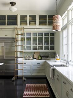 a ladder is in the middle of a kitchen with white cabinets and black flooring