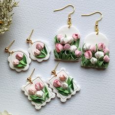 four pieces of jewelry with pink and white tulips on them, sitting next to flowers