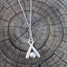 a silver letter necklace on a chain sitting on top of a piece of tree trunk