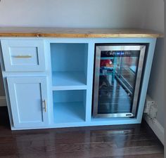 an empty refrigerator in the corner of a room with wood flooring and white cabinets