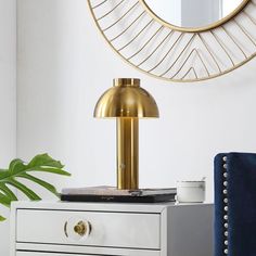 a gold lamp on top of a white dresser next to a blue chair