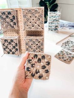 someone is holding up some crocheted coasters on a table in front of them