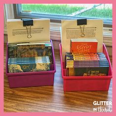 two pink bins with books in them sitting on a table next to a window