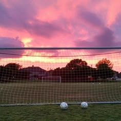 a soccer goal with three balls in front of it and the sun setting behind them