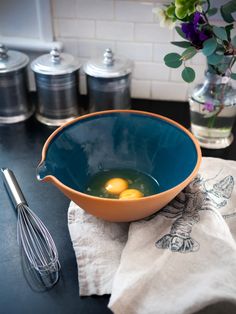 two eggs in a blue bowl on a kitchen counter next to a whisk