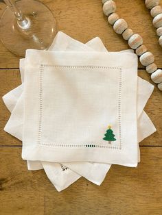 four white napkins with embroidered christmas tree on them next to a glass of wine