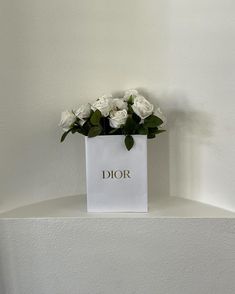 white roses in a paper bag sitting on top of a shelf with the word dior written on it