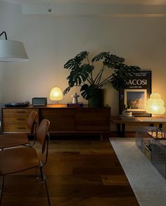 a living room filled with furniture and a plant on top of a wooden dresser next to a lamp