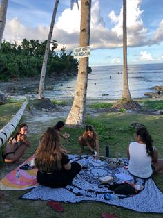 three women sitting on the grass near some palm trees and one woman is eating food